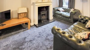 Una sala de estar con chimenea, un sofá de cuero, un banco de madera y una lámpara.