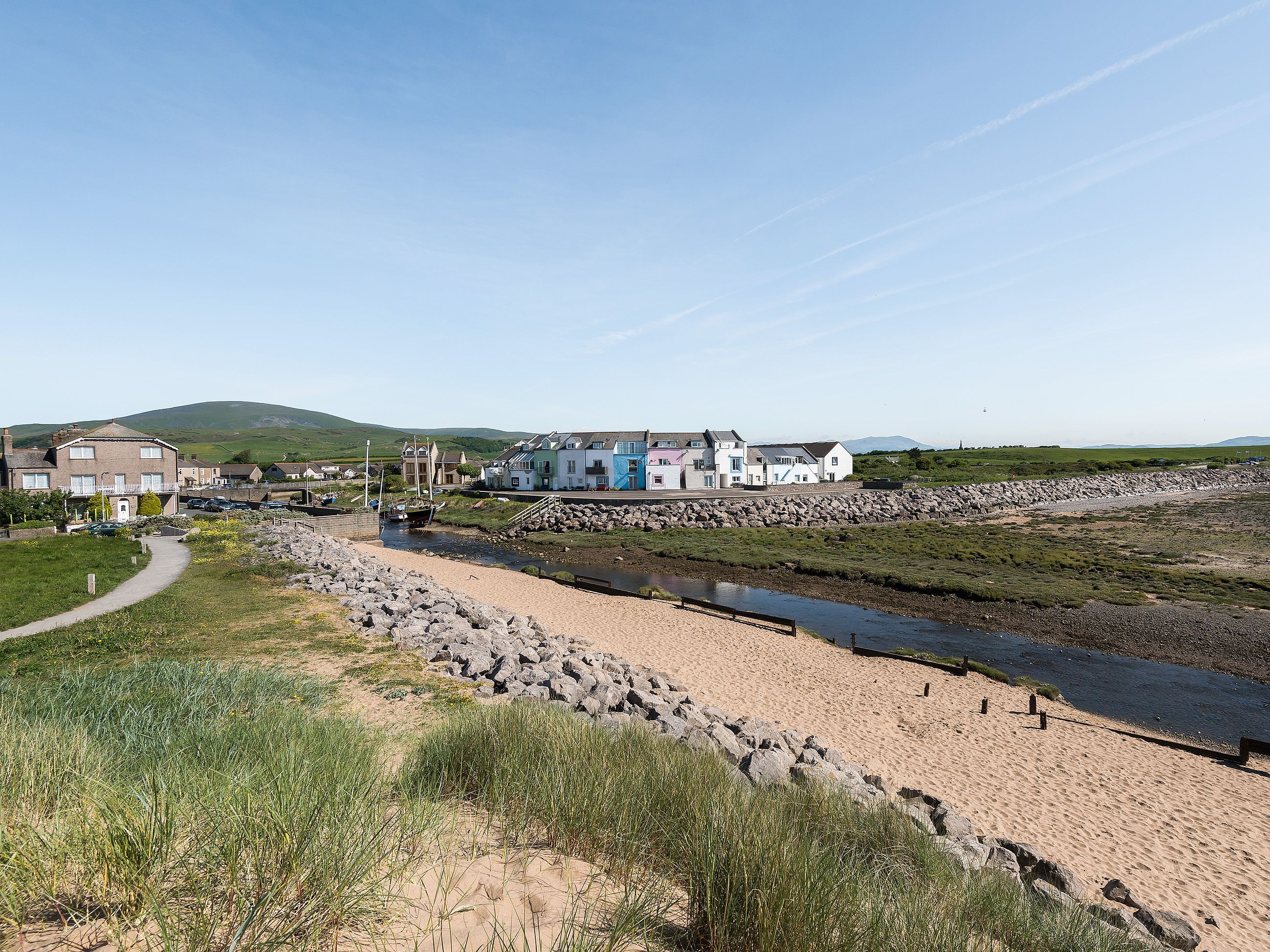 A coastal area with a river, a sandy beach, and a row of houses.