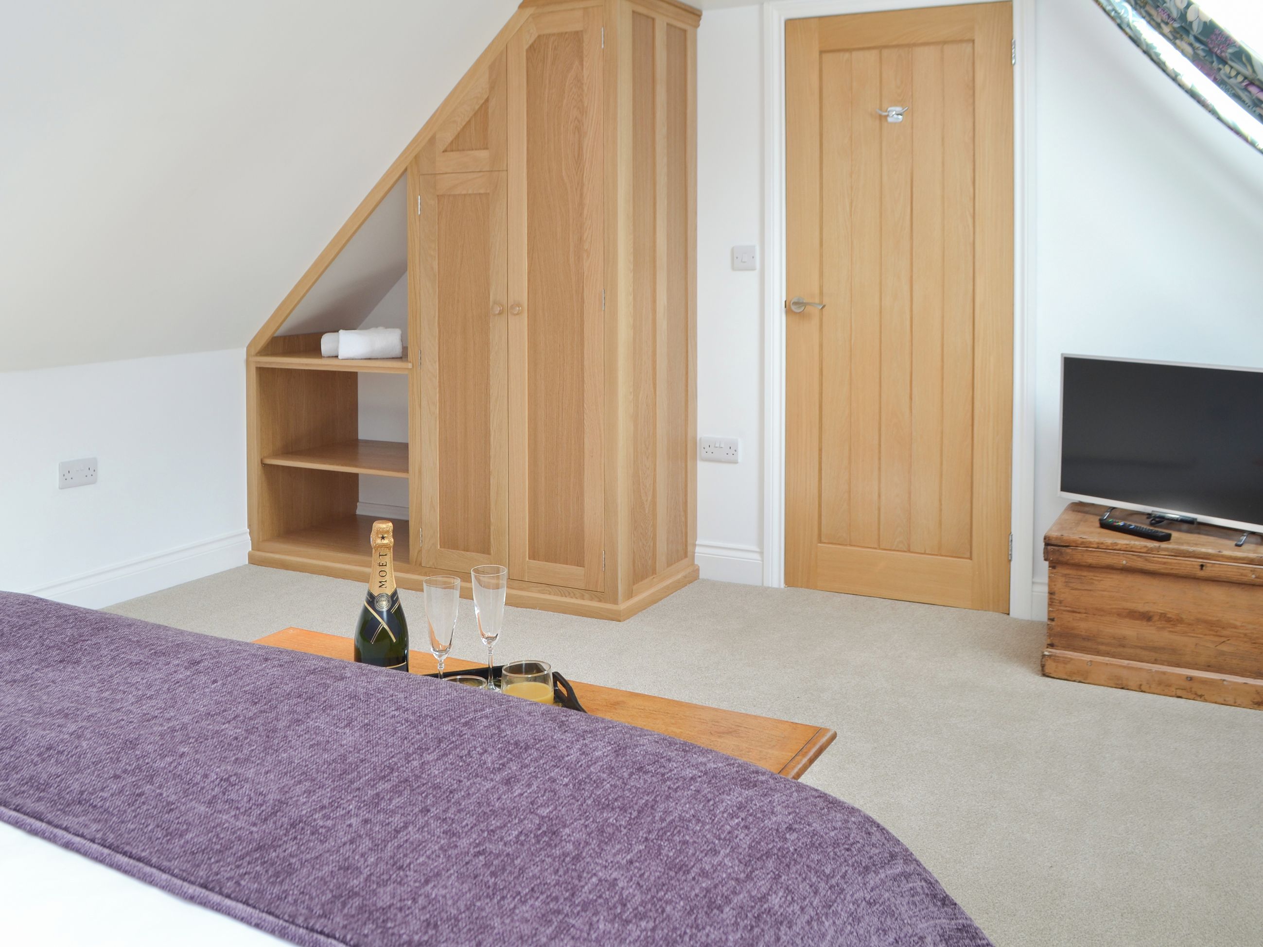 Une chambre à coucher avec un lit, une armoire en bois, une télévision et une petite table sur laquelle se trouvent des verres et une bouteille.