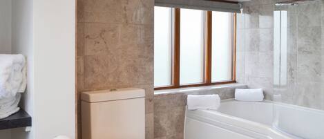 Une salle de bain moderne équipée de toilettes, d’une baignoire et d’une fenêtre avec des stores.