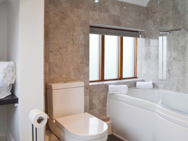 Un baño moderno con inodoro, bañera y ventana con persianas.
