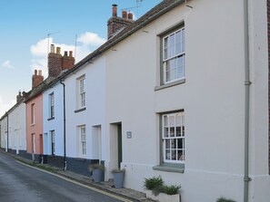 A row of terraced houses with white and pastel-colored facades, a clear sky, and a street with no visible traffic.
