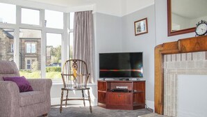 A living room with a sofa, a wooden chair, a television, and a fireplace. - 3 bedroom accommodation in Bakewell (Bakewell)