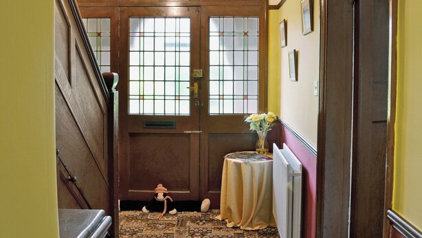A hallway with a wooden door, a radiator, a small table with a vase, and a staircase. - 3 bedroom accommodation in Bakewell (Bakewell)