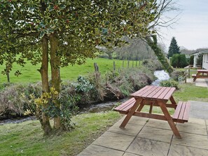 Une table de pique-nique dans un jardin, avec vue sur un champ verdoyant et un ruisseau.