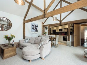A cozy living room with a curved sofa, a dining table, and a kitchen in the background. - 3 bedroom accommodation in Horning, near Wroxham (Horning, near Wroxham)
