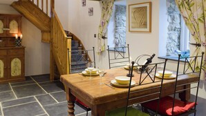 Comedor con mesa de madera dispuesta para dos, una escalera y una pared de piedra.