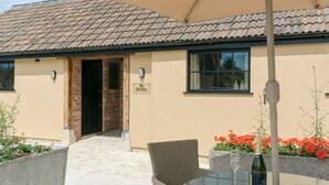 A building with a tiled roof, a sign reading 'The Old Dairy,' outdoor seating with a table, chairs, a glass, and a bowl of snacks. - The Old Dairy-UKC2112 (Royal Wootton Bassett)