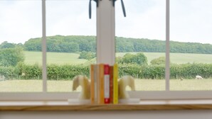 A window with a view of a green landscape, a white object in the foreground, and a metal structure on the window frame. - The Old Dairy-UKC2112 (Royal Wootton Bassett)
