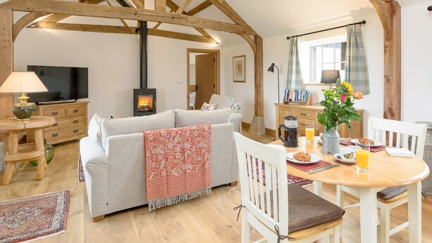 A cozy living room with a fireplace, sofa, dining table, and a TV. - The Old Dairy-UKC2112 (Royal Wootton Bassett)