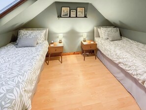 A bedroom with two beds, wooden nightstands, bedside lamps, a clock, and framed pictures on the wall.