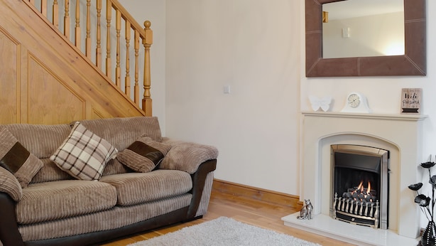 A living room with a wooden staircase, a fireplace, and a sofa with cushions. - 2 bedroom accommodation in Allonby, near Maryport (Allonby, near Maryport)