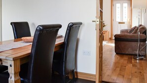 A dining area with a wooden table and black chairs, a clock on the wall, and a door leading to another room with a sofa and lamp. - 2 bedroom accommodation in Allonby, near Maryport (Allonby, near Maryport)