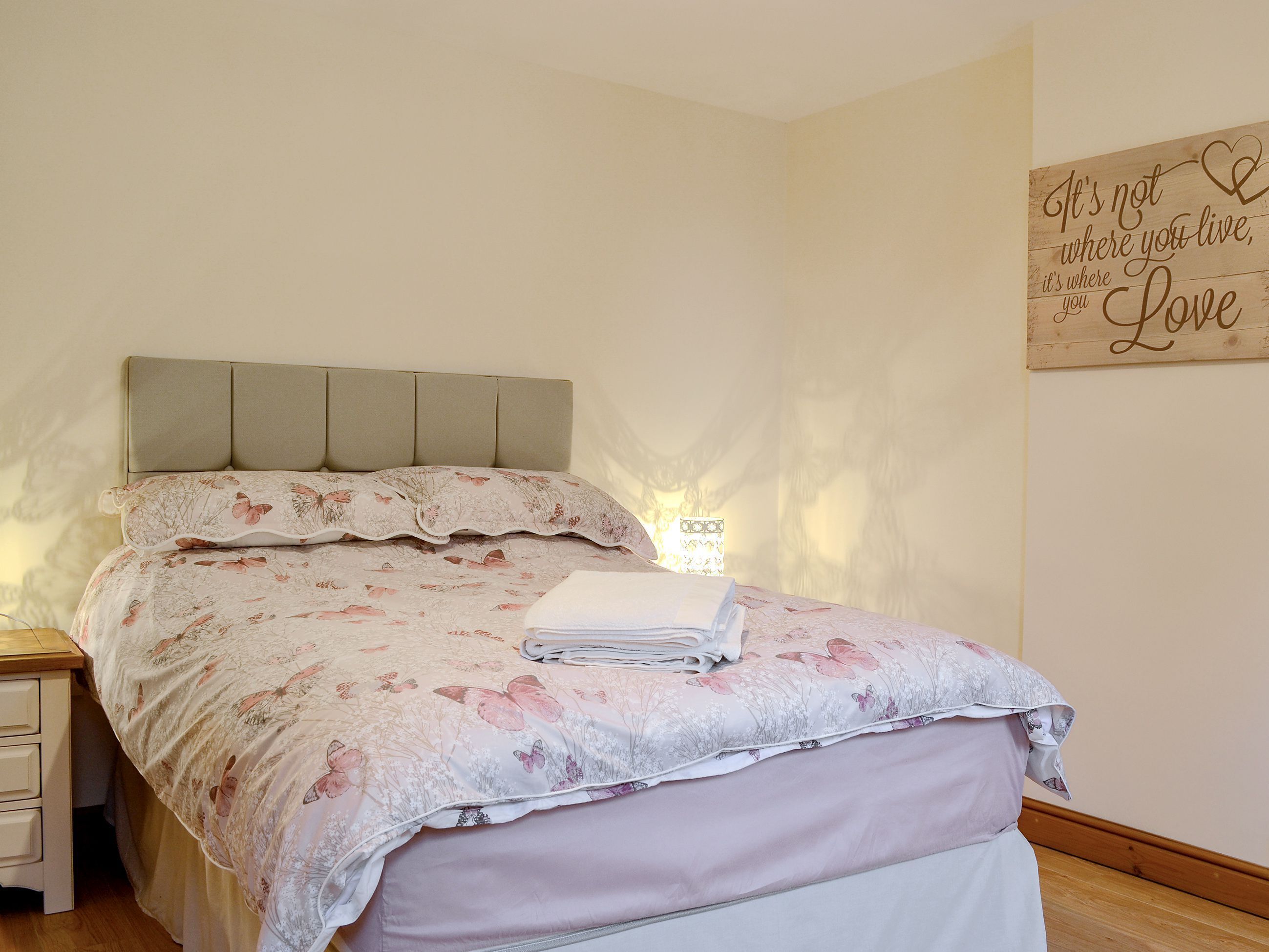 A bedroom with a bed, a bedside table, a nightstand, and a wall decoration.