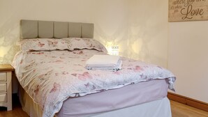A bedroom with a bed, a bedside table, a nightstand, and a wall decoration. - 2 bedroom accommodation in Allonby, near Maryport (Allonby, near Maryport)
