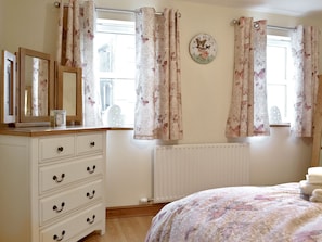 Un dormitorio con un aparador de madera, un reloj de pared redondo, cortinas con estampado floral y una cama con colcha estampada.