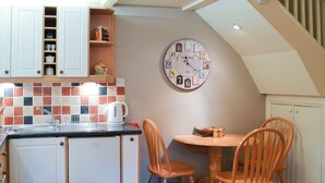 A compact kitchen with a dining area, featuring a clock on the wall, a kettle, and a coffee maker on the counter.