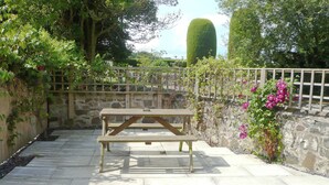 A stone patio with a wooden picnic table, surrounded by a stone wall and lush greenery.
