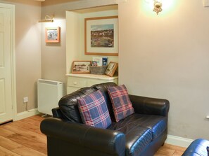 A living room with a black leather sofa, a white radiator, and framed pictures on the wall.