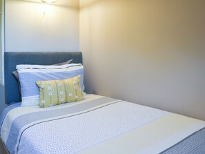 A neatly made bed with a blue headboard, a yellow pillow with white buttons, and a white and blue striped blanket.