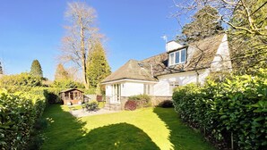 A well-maintained garden with a lawn, a small wooden structure, and a white house with a stone foundation. - 3 bedroom accommodation in Bowness-on-Windermere, near Windermere (Bowness-on-Windermere, near Windermere)