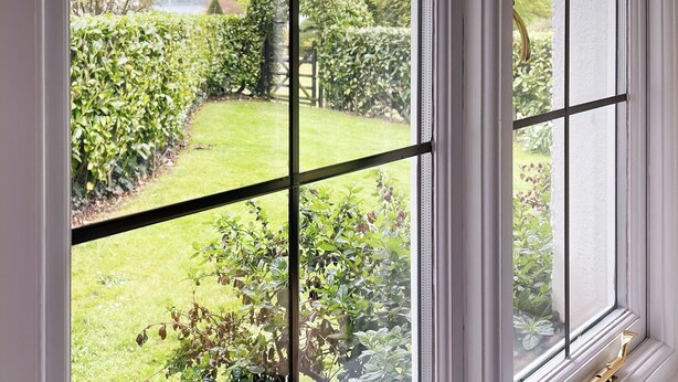 A view through a window with a grid pattern, revealing a well-maintained garden with various plants and a lawn. - 3 bedroom accommodation in Bowness-on-Windermere, near Windermere (Bowness-on-Windermere, near Windermere)