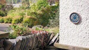 A stone wall with a plaque reading "Granton Lodge" and a view of a lush landscape with trees and a distant body of water. - 3 bedroom accommodation in Bowness-on-Windermere, near Windermere (Bowness-on-Windermere, near Windermere)