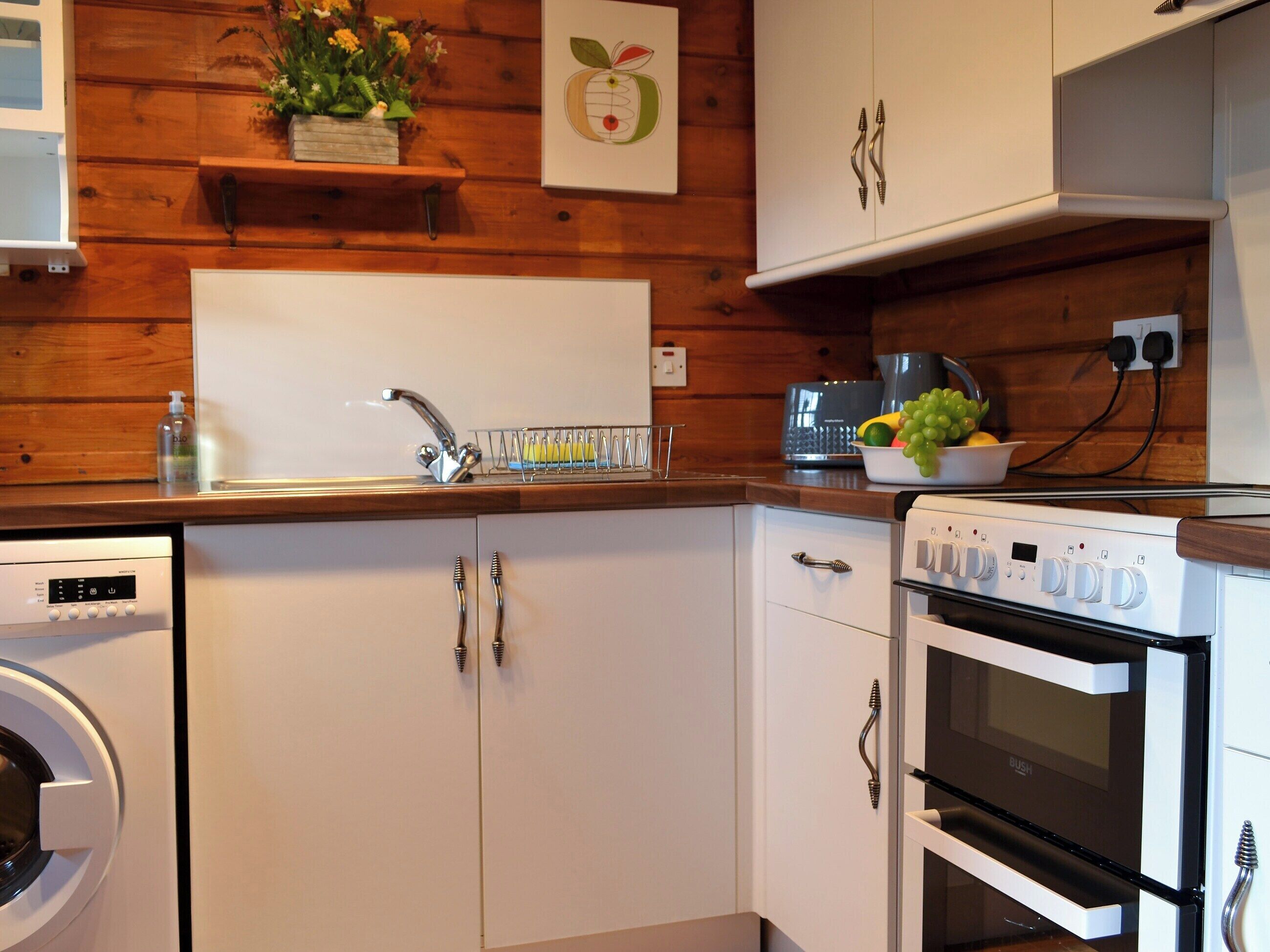 Une cuisine avec des meubles de rangement en bois, un lave-vaisselle, un four et un panier à fruits posé sur le plan de travail.