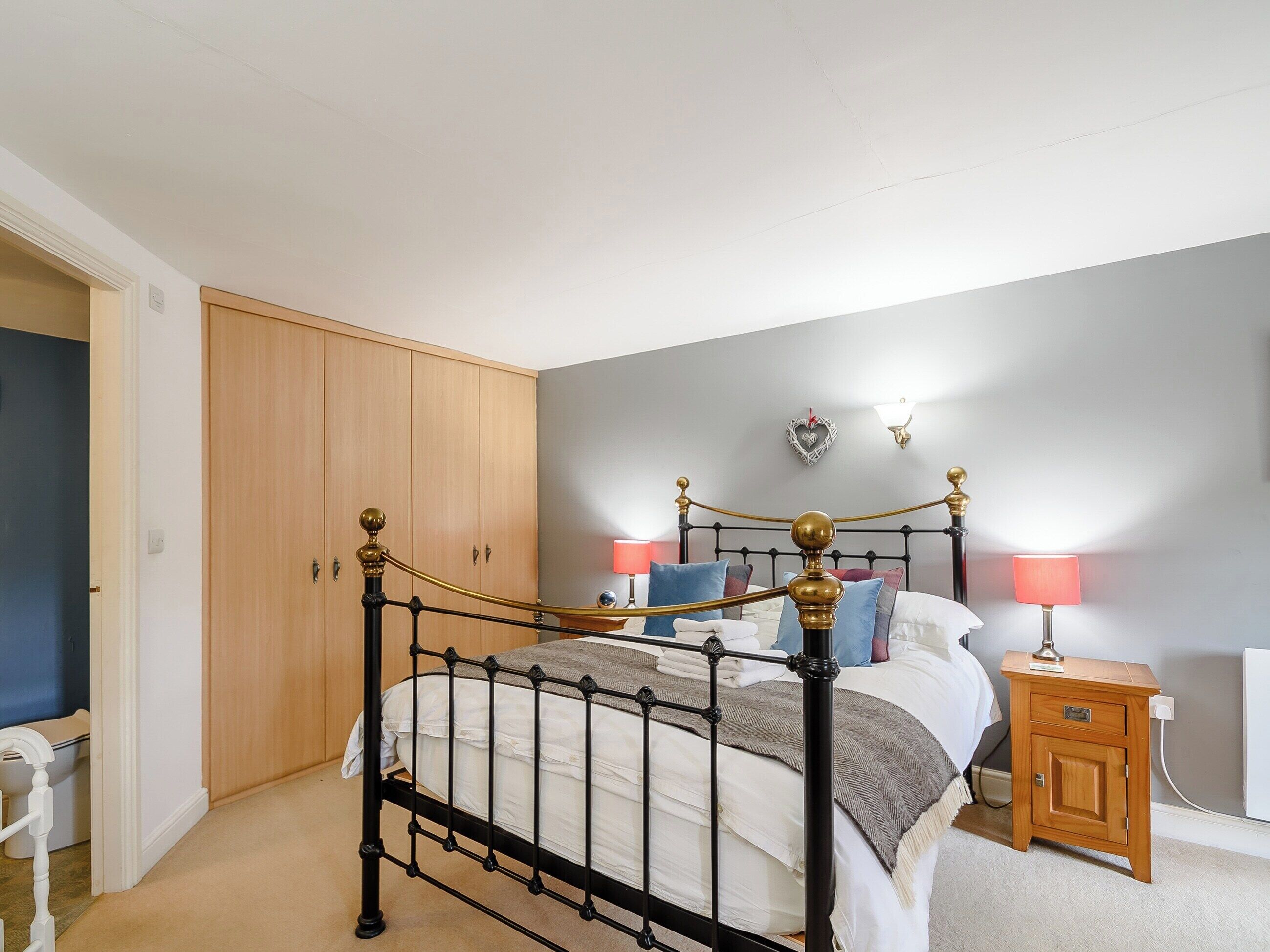 A bedroom with a four-poster bed, wooden wardrobe, bedside table, and a wall-mounted lamp.