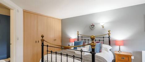 A bedroom with a four-poster bed, wooden wardrobe, bedside table, and a wall-mounted lamp.