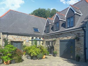 A house with a stone facade, a grey tiled roof, and a garage. - 2 bedroom accommodation in Plympton, near Plymouth (Plympton, near Plymouth)
