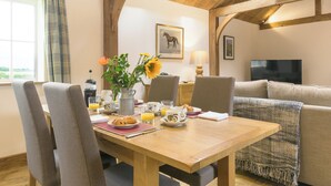A dining area with a wooden table, chairs, and a vase with flowers. - The Calf Shed-UKC2113 (Royal Wootton Bassett)