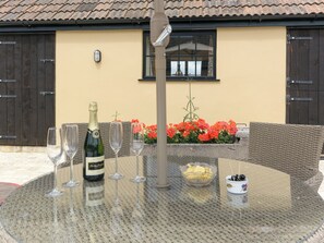 Une table ronde en verre, avec une bouteille de champagne, deux verres, un bol de collations et un petit objet décoratif.