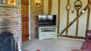 A living room with a brick fireplace, a television on a white stand, a red rug, and a leather sofa.