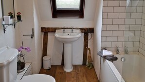 A bathroom with a white sink, a window, a wooden beam, a toilet, a trash can, and a bathtub.