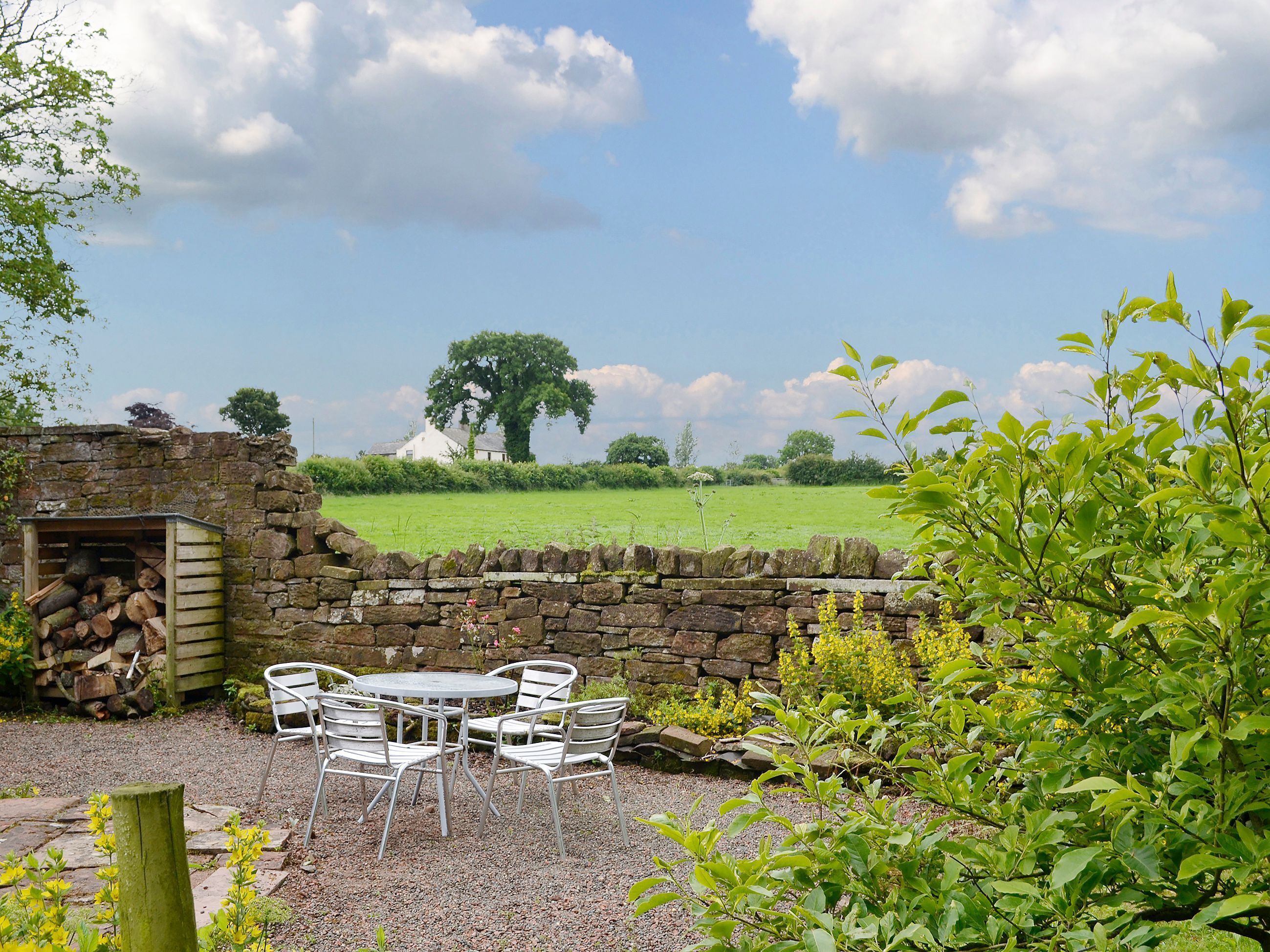 A stone wall with a rustic wooden table and metal chairs in a garden setting.
