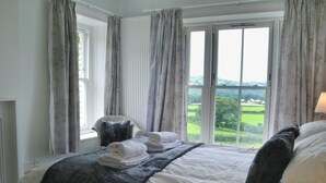 A bedroom with a large bed, a chair, and a view of a green landscape through the window. - 4 bedroom accommodation in Capel Bangor, near Aberystwyth (Capel Bangor, near Aberystwyth)