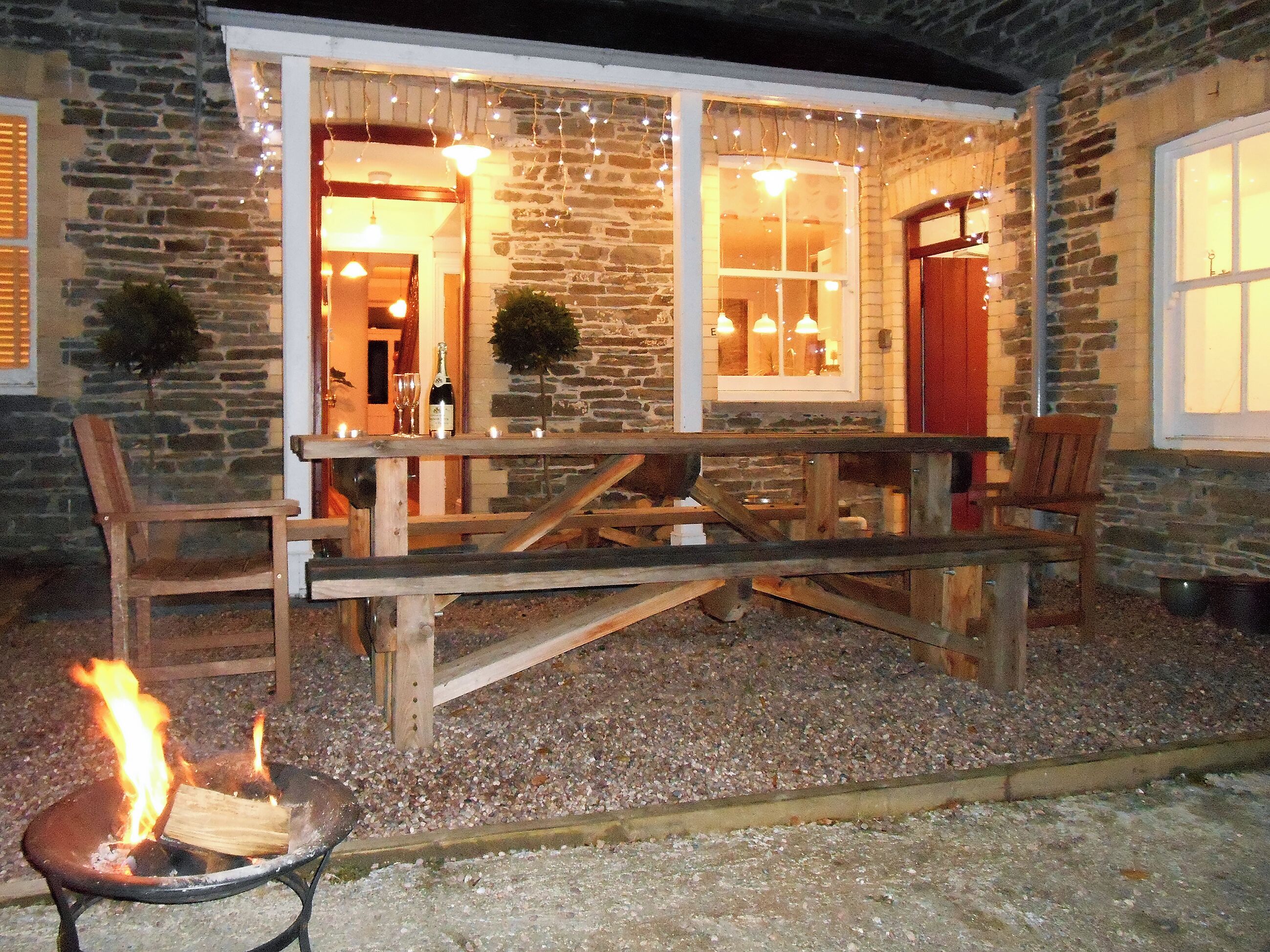A stone building with a wooden deck, outdoor seating, and a fire pit.