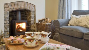 A cozy living room with a stone fireplace, a wicker basket, a grey sofa, and a table with tea sets and pastries. - 4 bedroom accommodation in Capel Bangor, near Aberystwyth (Capel Bangor, near Aberystwyth)
