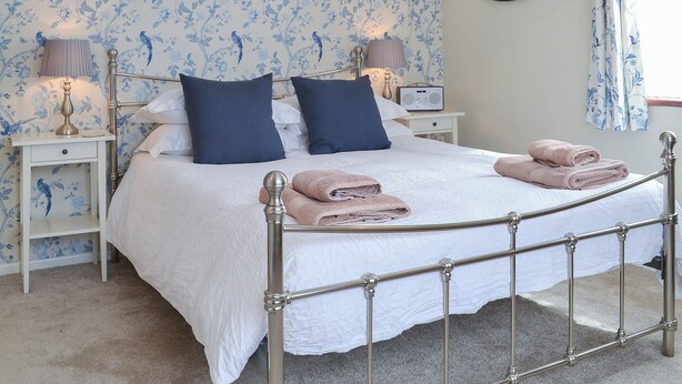 Een keurig opgemaakt bed met twee kussens, een nachtkastje met een lamp en een radio.