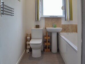 Ein kleines Badezimmer mit Toilette, Waschbecken und einem Fenster mit gestreifter Vorhang.