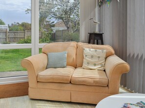 A beige sofa with two pillows, a window with a view of a backyard, and a small table with magazines. - 2 bedroom accommodation in Mundesley, near North Walsham (Mundesley, near North Walsham)
