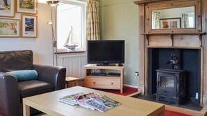 Een woonkamer met een leren bank, een houten salontafel met tijdschriften, een televisie op een meubel, een open haard en een raam met gordijnen.