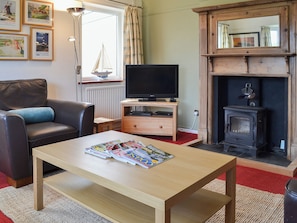 Uma sala de estar com um sofá, uma mesa de centro de madeira com revistas, uma televisão sobre um móvel de madeira, uma lareira e uma janela com cortinas.