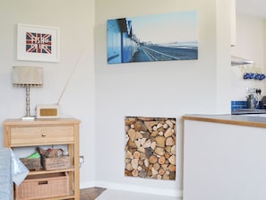 Um quarto com mesa de cabeceira de madeira, um rádio, um quadro emoldurado, um quadro pendurado na parede e uma pilha de lenha.