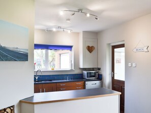 A modern kitchen with a built-in microwave, a sink, and a window with blue blinds. - 2 bedroom accommodation in Mundesley, near North Walsham (Mundesley, near North Walsham)