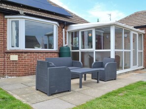 A patio with wicker furniture, a conservatory, and a brick house. - 2 bedroom accommodation in Mundesley, near North Walsham (Mundesley, near North Walsham)