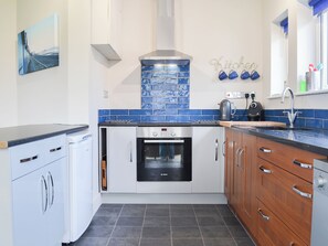 Cocina compacta con armarios blancos, horno Bosch, salpicadero de azulejos azules y una pequeña zona de café.