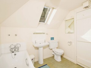 A small, white bathroom with a skylight, a toilet, a sink, and a bathtub.