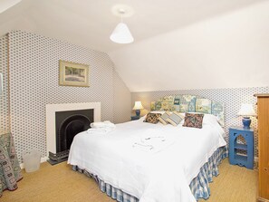 A bedroom with a bed, a fireplace, patterned wallpaper, and a hanging light fixture.